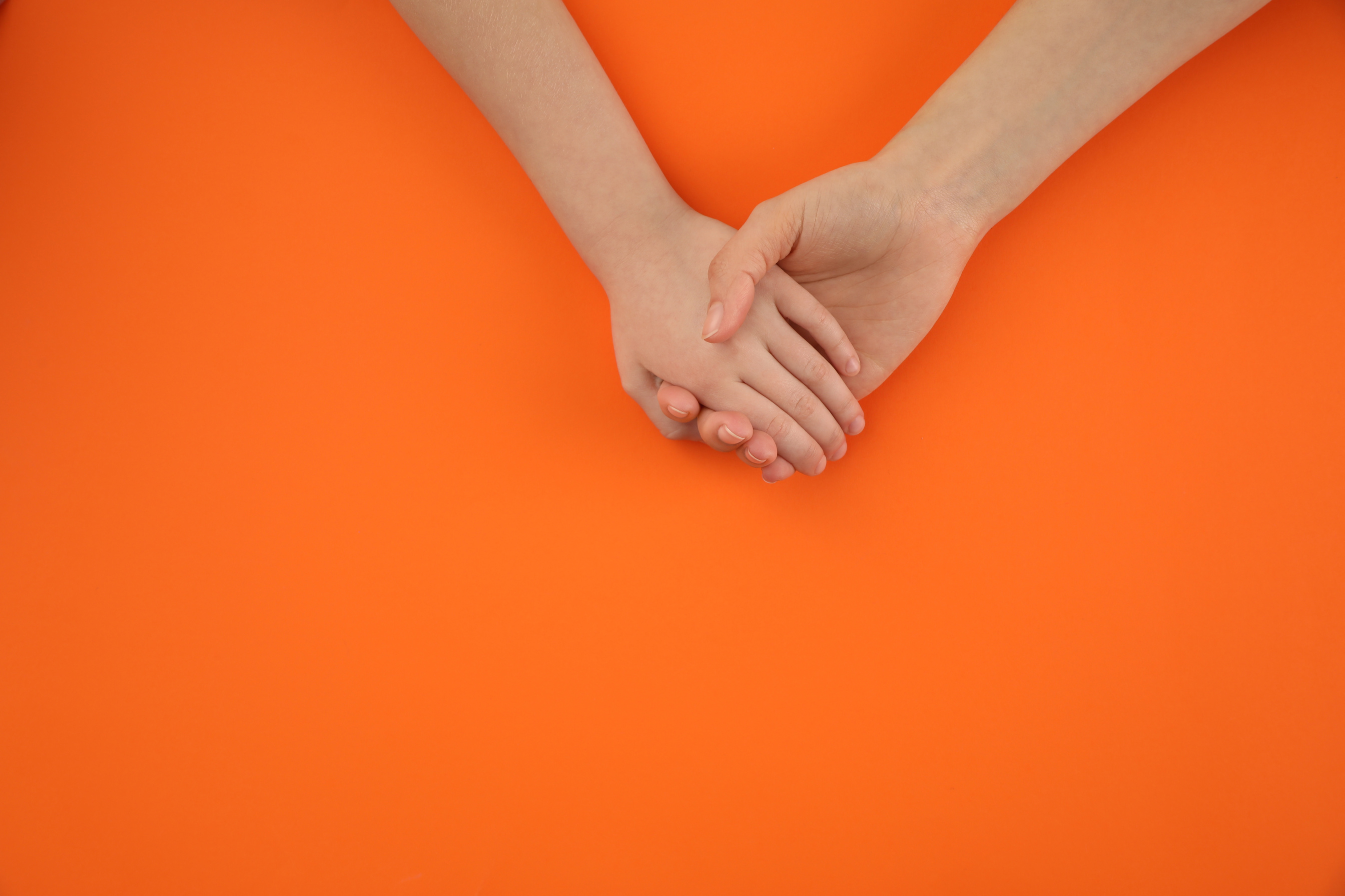 Mother Holding Hands with Her Child on Orange Background, Top View. Happy